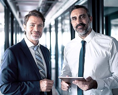 Store headquarters want stability, security, and smooth processes for their site networking Two businessmen in suits and holding tablets stand in office buildings and look confidently into the camera